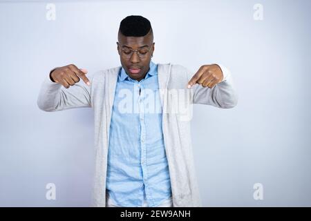 Young handsome african american man wearing casual clothes surprised, looking down and pointing down with fingers and raised arms Stock Photo