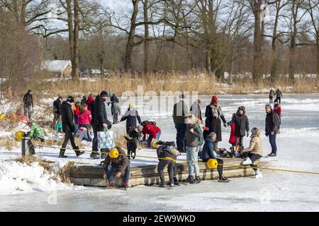 ZUTPHEN, NETHERLANDS - Feb 14, 2021: Gathering of people at the edge of a frozen riverbed arriving or preparing to go ice skating Stock Photo