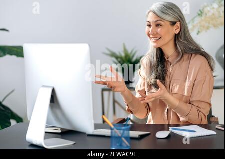 Happy mature asian woman communicate by video call on computer working from home. Smiling middle aged businesswoman talking by video conference, online virtual meeting using computer Stock Photo