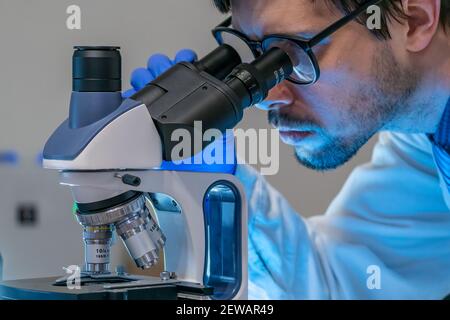 Young scientist in laboratory is looking inside microscope. Stock Photo