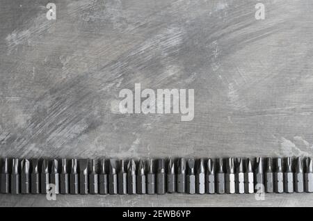 Screwdriver bits for various slots laid out in a row on a gray concrete surface. Stock Photo
