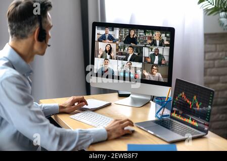 Business meeting online. Successful businessman is negotiating with multiracial business partners on a video conference using a computer while sitting at his workplace Stock Photo