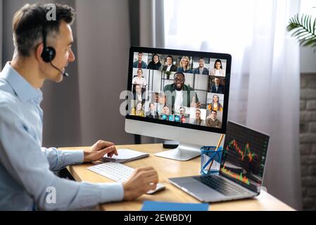 Business meeting online. Successful businessman is negotiating with multiracial business partners on a video conference using a computer while sitting at his workplace Stock Photo