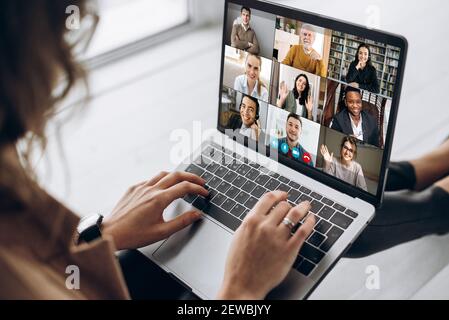 Back view of female employee communicate on video call with multiracial colleagues, woman worker conducts webcam group conference with business partners uses laptop and app Stock Photo
