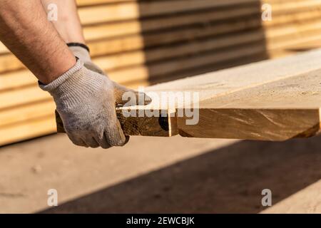 Close up on hands with working gloves of unknown caucasian man construction worker picking wood planks timber at warehouse in sunny day with copy spac Stock Photo