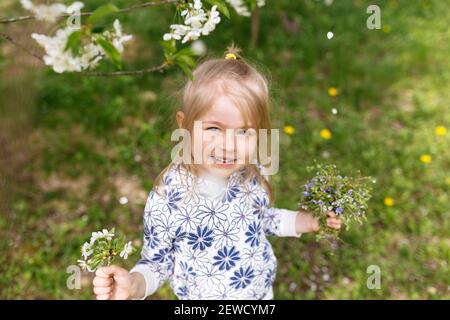 Little girl with spring flowers on green lawn in the garden. High quality photo Stock Photo