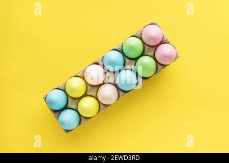 Easter colored eggs in egg carton on yellow background with copy space for text. Stock Photo
