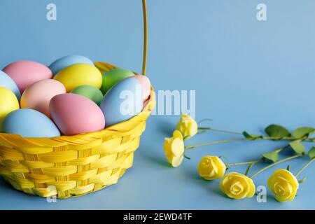 Easter eggs in basket with small flowers aside and copy space on blue background. Easter composition. Stock Photo