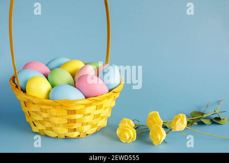 Easter eggs in basket with small flowers aside and copy space on blue background. Easter composition. Stock Photo
