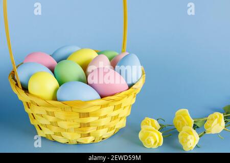 Easter eggs in basket with small flowers aside and copy space on blue background. Easter composition. Stock Photo
