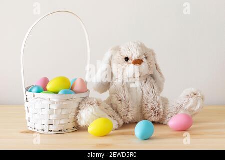 Easter toy bunny, colored eggs with basket on wooden table with white background and copy space. Stock Photo