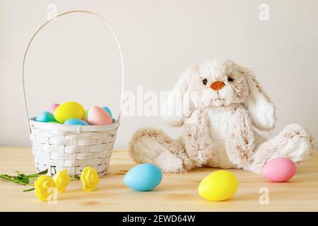 Easter toy bunny, colored eggs with basket on wooden table with white background and copy space. Stock Photo