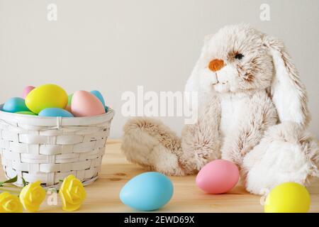 Easter toy bunny, colored eggs with basket on wooden table with white background and copy space. Stock Photo