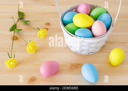 Colored eggs with basket and small flowers on wooden table with copy space for text. Stock Photo