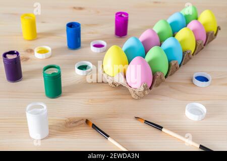 Easter eggs and colored paints with paintbrushes on the table. Easter craft concept. Stock Photo
