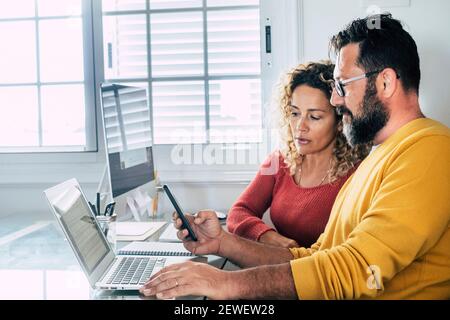Smart working at home free office lifestyle with adult couple using home and two pc laptop computer on the desktop - modern man and woman online job r Stock Photo