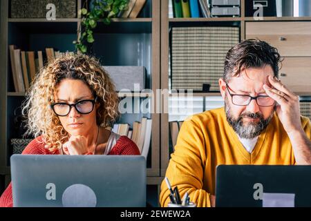 Stressed and tired couple at work at home with laptop internet computer connection - concept of smart working and modern people lifestyle - man and wo Stock Photo