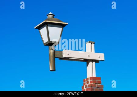 Decorative lamp post with lantern head and white glass on wooden pole and brick base. Blue sky. Stock Photo