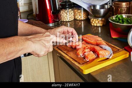 Cooking at home in the kitchen according to recipe from the Internet. Woman cuts fresh salmon with knife on cutting board. Step by step recipe Stock Photo