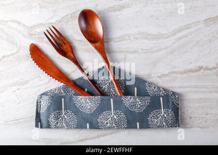 Close up isolated flat lay image of a wooden cutlery set consisting of a soup spoon, a salad fork and a table knife sticking out of a decorative fabri Stock Photo
