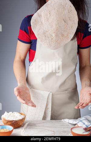 Preparation of homemadeTurkish flat bread, pide or pizza base in the kitchen. The female baker is throwing the kneaded and flattened base in the air f Stock Photo