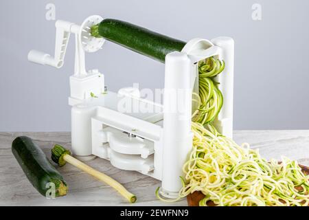 Close up isolated image of a plastic hand operated vegetable slicer, spiralizer on kitchen countertop. Image shows zucchini noodles being made passing Stock Photo