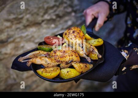 From above of crop anonymous chef with appetizing poultry near golden potato with tomato slices on grill pan Stock Photo