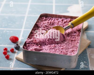 From above of appetizing ice cream scoop in metal container on cutting board near fresh juicy red berries and blueberry Stock Photo