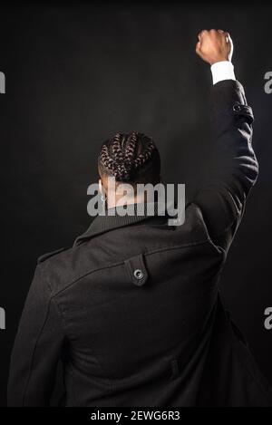 Black man from behind with raised fist. Mid shot. Black background. Stock Photo