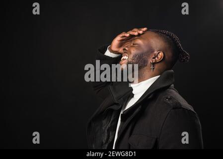 Black man in profile laughing with his hand on his face. Close up. Black background. Stock Photo
