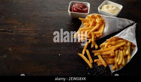 From above of appetizing golden fried potato sticks near bowls with ketchup and mayonnaise on wooden table Stock Photo