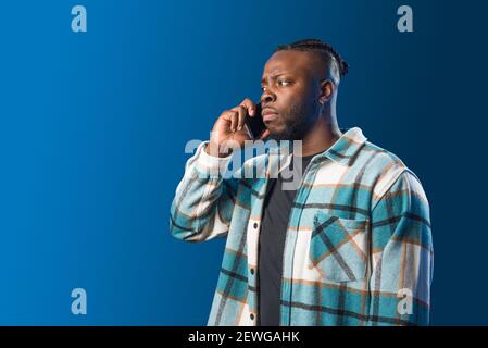 Handsome black man talking on the mobile worried. Mid shot. Blue background. Stock Photo