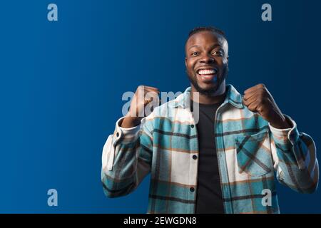 Handsome black man smiling, celebrating something with his fists raised. Blue background Stock Photo