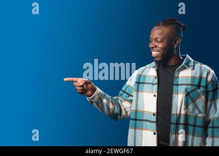 Handsome black man pointing aside, smiling. Mid shot. Blue background. Stock Photo