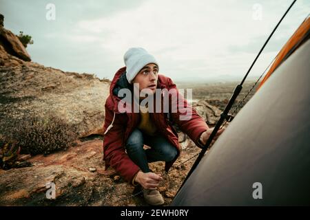 Caucasian male hiker pitching tent on mountain peak camping outdoors with friends Stock Photo