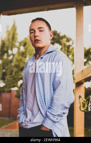 A vertical portrait of an attractive European man in a casual shirt posing outdoors in a garden Stock Photo