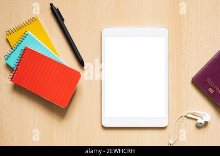 Flat lay with copy space, some office supply, passport and a tablet with white screen are arranged on a wooden table. Stock Photo