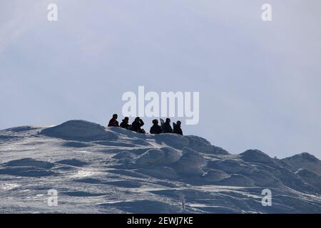 Silhouettes of a  group of snowboarders sitting on a mountain top Stock Photo