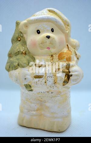 White ceramic statuette of a Christmas teddy bear in a Christmas hat with a golden christmas tree and gifts in hand. Stock Photo