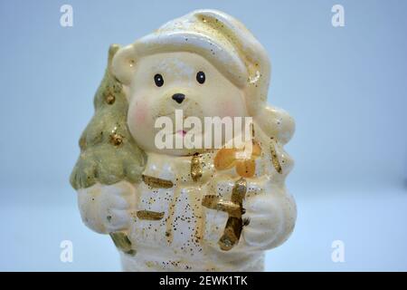 White ceramic statuette of a Christmas teddy bear in a Christmas hat with a golden christmas tree and gifts in hand. Stock Photo