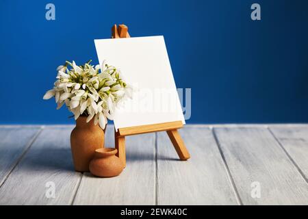 Bouquet of Galanthus flowers and a small easel with a white paper a on a wooden background. Greeting card with a copy space Stock Photo