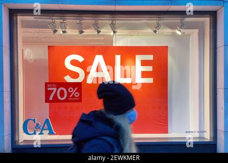 Hamburg, Germany. 31st Dec, 2020. A woman wearing a mouth-to-nose mask walks past the window of a store downtown with a notice advertising a discount of up to 70 percent. Credit: Soeren Stache/dpa-Zentralbild/ZB/dpa/Alamy Live News Stock Photo
