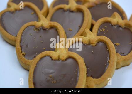 Delicious and sweet shortbread apple-shaped cookies with brown chocolate nut filling located on a white background. Stock Photo