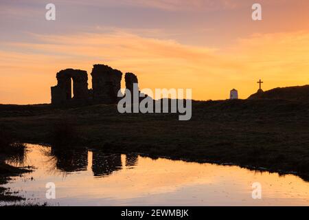 St Dwynwen's church ruins and orange sky reflected in a pool of water at sunset on Llanddwyn Island, Newborough, Isle of Anglesey, Wales, UK Stock Photo