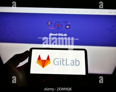 High angle view of person holding mobile phone with logo of US DevOps platform GitLab Inc. on screen in front of website. Focus on cellphone display. Stock Photo