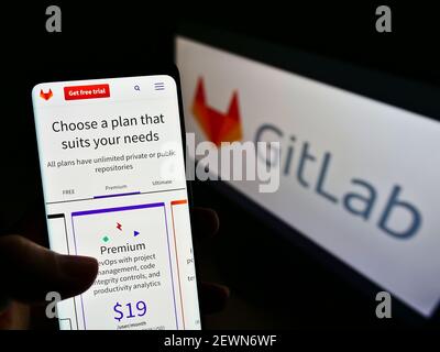 Person holding cellphone with web page of US DevOps software platform GitLab Inc. on screen in front of logo. Focus on center of phone display. Stock Photo