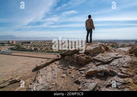 Iranian man in slimfit jacket overlooking Iranian city of Yazd from the hill of tower of silence. Hot sunny day in Yazd, Iran. Stock Photo