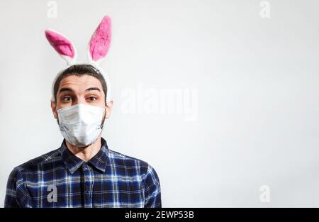 Caucasian man with pink hare ears wears medical protective mask. Empty space for text or ad on white background. Man with ears of Easter bunny. Stock Photo