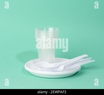 disposable white plastic tableware plates, cups, forks and knives on a green background, picnic set Stock Photo