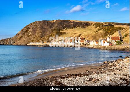 CROVIE VILLAGE ABERDEENSHIRE SCOTLAND A ROW OF HOUSES WITH RED ROOF TILES A BLUE SKY AND A WAVE BREAKING OVER THE SAND AND PEBBLE BEACH